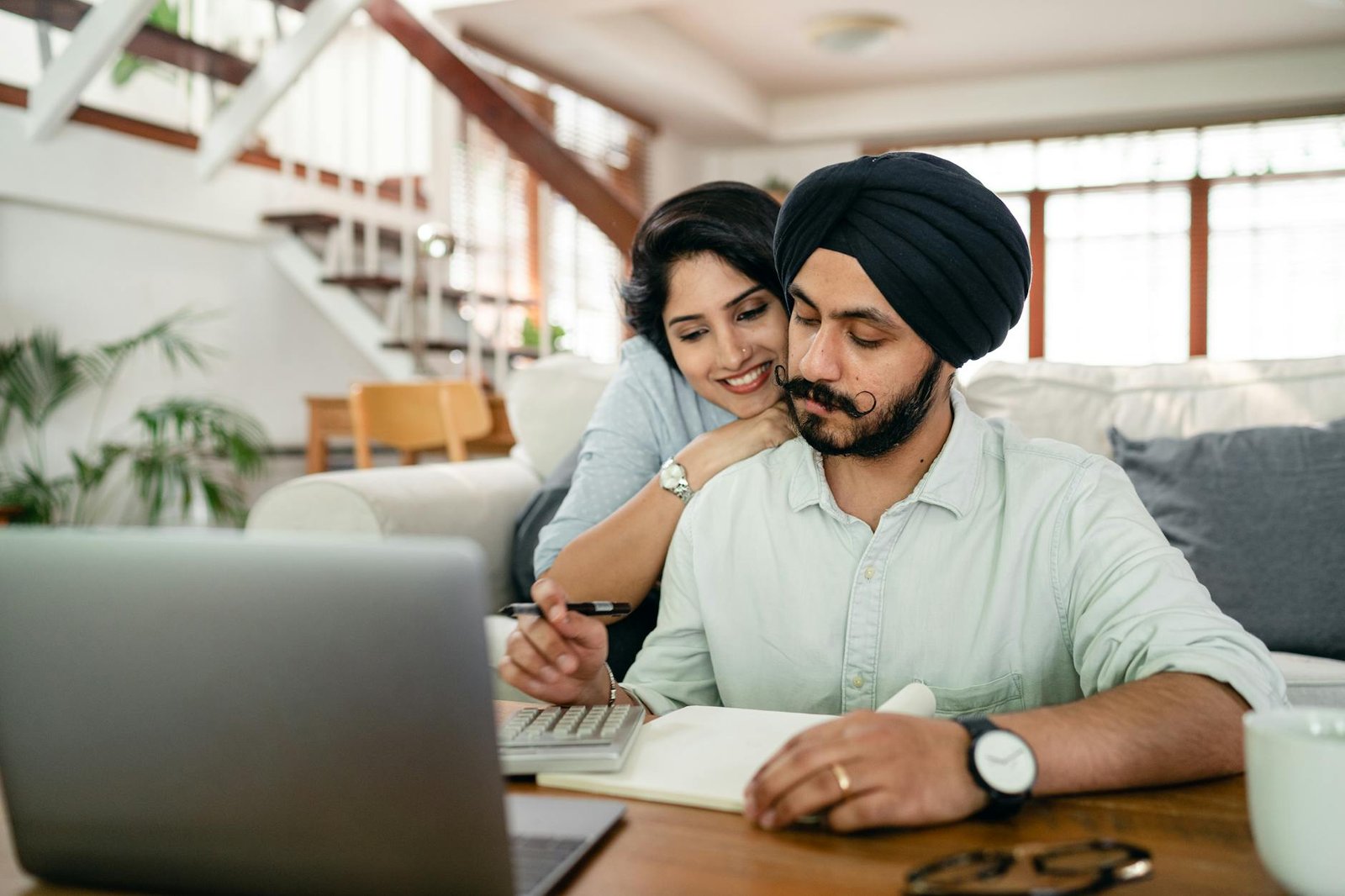 photo/serious-young-sikh-man-with-hugging-wife-counting-on-calculator-at-home-4308052/